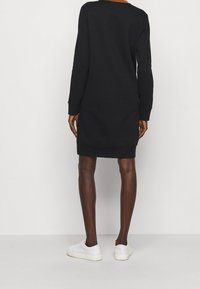 Svart sweatshirtklänning med långa ärmar, ribbade muddar och rundad halsringning. Bärs med vita sneakers. Slät yta, avslappnad design.