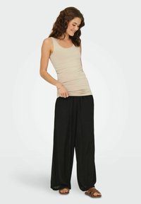 Beige, åtsittande linnetopp i kombination med lösa svarta byxor, som har en slät textur och vid bendesign. Bruna sandaler fulländar outfiten.