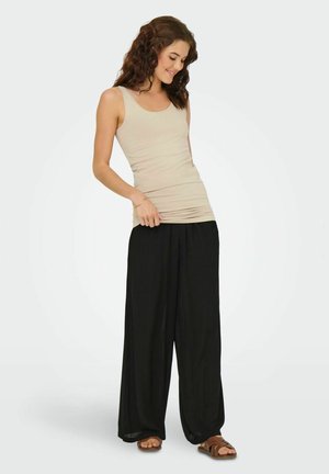 Beige tætsiddende tanktop parret med løse sorte bukser, der har en glat tekstur og bred ben-design. Brune sandaler fuldender antrekket.