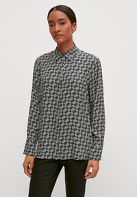 Black and white patterned long-sleeve shirt with a collar, featuring a geometric design. The fabric appears smooth and lightweight.