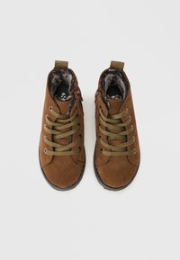 Brown suede ankle boots with green laces, a soft fur lining, and a textured rubber sole. Features a zipper on the side for easy wear.