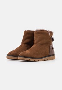 Bottines en daim marron avec une doublure intérieure en fausse fourrure douce, un accent texturé marron sur le côté, et une semelle extérieure en caoutchouc avec un motif de bande de roulement.