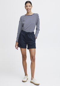 Mörkblå shorts med elastisk midja och uppvikta ärmar, ihop med en långärmad skjorta i mörkblått och vitt randigt mönster. Vita sneakers.