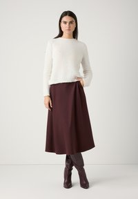 Weißer, flauschiger Pullover mit langen Ärmeln, kombiniert mit einem bordeauxfarbenen, knielangen, plissierten Rock und braunen Stiefeln bis zum Knie. Schlichtes Design und Texturen.