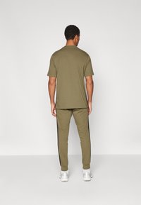 Kaki bomull T-skjorte og matchende joggebukser med sorte sidestiper; avslappet passform; ensfarget design; båret med hvite sportssko.