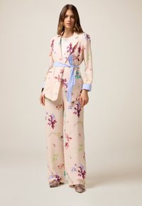 Completo in tessuto leggero a fantasia floreale in rosa pallido, dotato di giacca sartoriale con polsini blu, cintura a nodo e pantaloni a gamba larga.