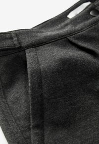 Gros plan sur un pantalon en laine gris foncé montrant la taille, une boucle de ceinture, un bouton et une poche latérale avec des coutures détaillées et la texture du tissu.