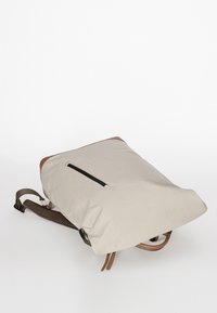 Beige backpack made of waterproof material, featuring brown leather accents and a front zip pocket. Includes adjustable fabric straps.