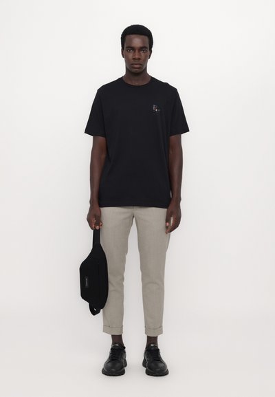 Tricou din bumbac negru cu mâneci scurte, asociat cu pantaloni scurți gri deschis cu croială ușor conică. Modelul ține o geantă neagră. Design simplu, fără modele vizibile.