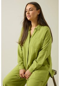 Camisa de lino verde y pantalones a juego, con un diseño de botones, bolsillo frontal y corte relajado. La tela tiene un aspecto texturizado.
