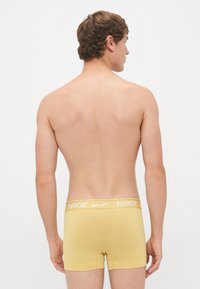 Geel katoenen boxershorts met een witte Nike tailleband, van achteren gezien, met een getailleerd ontwerp en een gladde textuur.