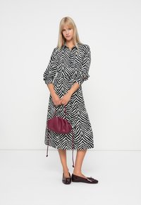 Μαύρο και άσπρο φόρεμα με ρίγες από ζέβρα, μακρυά μανίκια, σφιγμένη μέση και φουσκωτή φούστα. Συνοδεύεται από μάρσσιπο τσάντα χρώματος μπορντό με κορδόνια και γυαλιστερές μπαλαρίνες.