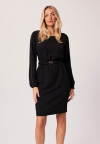 Czarna sukienka z długim rękawem i ściśniętą talią, z okrągłym dekoltem oraz dekoracyjnym przeszyciem na rękawach. Gładka struktura materiału.
