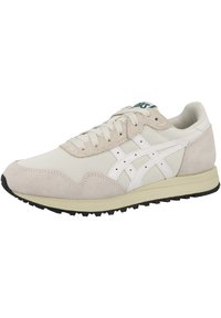 Zapatilla deportiva beige que presenta una mezcla de materiales de malla y ante, con acentos en blanco, punta redondeada y una suela de goma negra con relieve.
