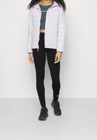 Giacca gonfiabile viola chiaro con chiusura a zip, leggings neri e scarpe da ginnastica nere. Presenta un top grigio corto e un cappuccio.