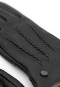 Schwarzer Lederhandschuh mit drei gesteppten Linien auf der Rückseite, weicher Textur und einem kleinen, runden Metallakzent nahe dem Bund.