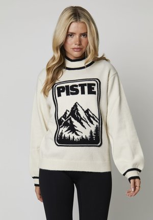 Jersey de punto color crema con gráfico de montaña negra y el texto "PISTE". Presenta un cuello alto y puños acanalados con franjas en contraste.