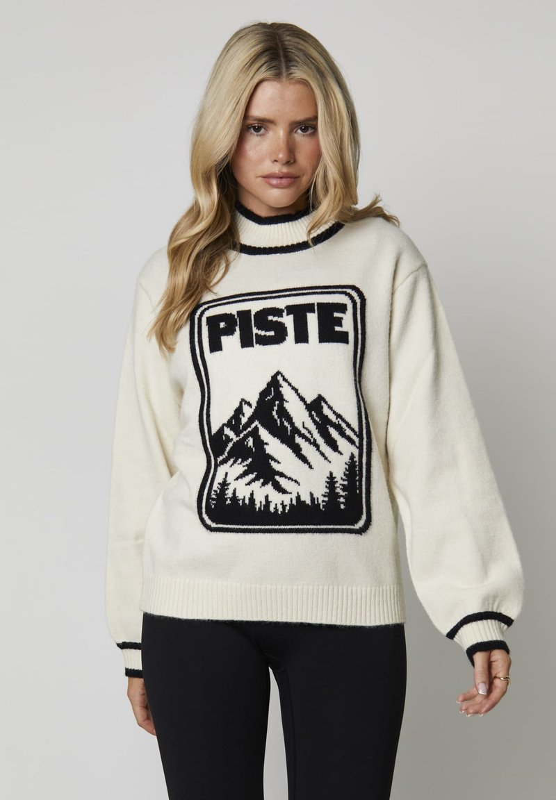 Crème-kleurige gebreide trui met een zwart bergafbeelding en "PISTE" tekst. Beschikt over een hoge kraag en geribde manchetten met contrasterende strepen.