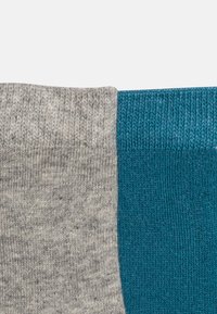 Socken mit einem geteilten Design, eine Seite hellgrau mit strukturiertem Strick und die andere Seite ein einheitliches Teal mit einem gerippten Strickfinish.