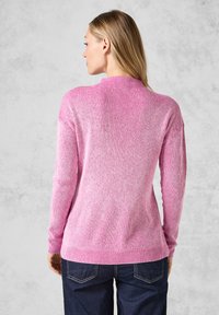 Rosa ribbad stickad tröja med långa ärmar och hög krage, som har en något avslappnad passform och en strukturerad tygmönster.