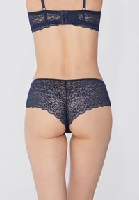 Námořnická modrá krajková souprava prádla s květinovými vzory, scalloped okraji a nastavitelnými ramínky na podprsence, doplněná o odpovídající krajkové kalhotky typu boyshort.