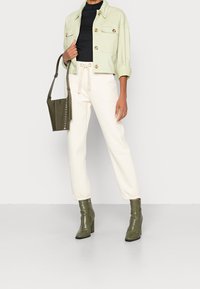 Světle zelená zkrácená bunda, černý přiléhavý top, krémové tepláky a olivově zelené boty na podpatku. Doplňky zahrnují texturovanou olivovou tašku.