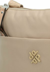 Beige Nylon Tasche mit glatter Textur, ausgestattet mit einem Reißverschluss und einem auffälligen, hellen Logoakzent auf der Vorderseite.