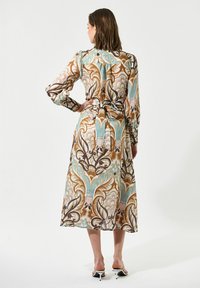 Vestito lungo multicolore con motivi floreali e astratti. Tessuto trasparente, dettaglio in vita annodato e maniche lunghe. La palette di colori include marrone, blu e crema.