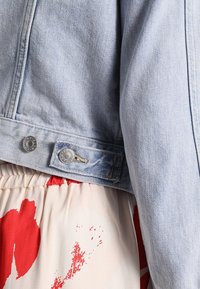 Svetlemodrá džínová bunda má stříbrné knoflíky a prošití a je kombinována s květinovým vzorem v červené a krémové barvě.