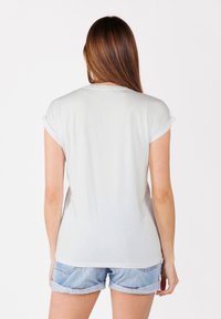 Hellgraues Kurzarm-T-Shirt mit aufgerollten Ärmeln, weicher Textur, leicht abgerundetem Saum und lässiger Passform. Kombiniert mit Jeansshorts.