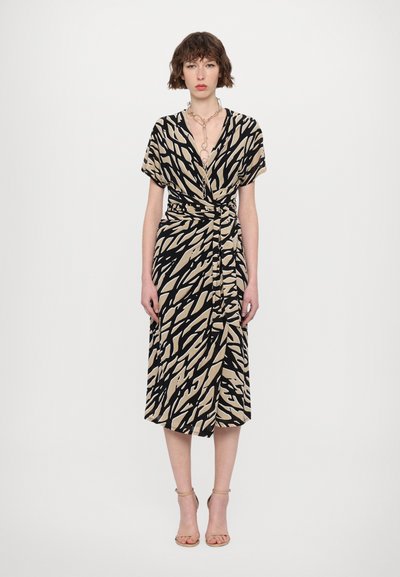 Vestido envolvente de manga corta en negro y beige con un patrón abstracto, con una cintura ceñida y un dobladillo a media longitud. Combinado con sandalias de tacón.