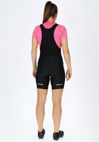 Svarta cykelshorts med bib-design, som har ett åtsittande snitt och reflekterande ränder på underbenen, samt en texturerad, andningsbar rosa topp.