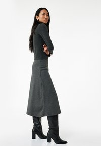 Grå strikket sweater parret med en matchende lang nederdel. Modellen bærer elegante sorte knæhæle støvler. Struktureret stof med lodrette mønstre.