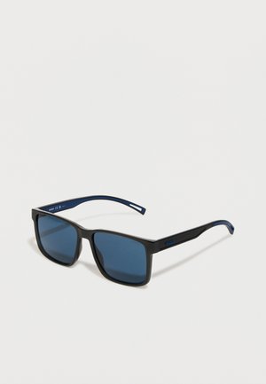 Gafas de sol con montura de plástico negro, lentes de tono azul, diseño cuadrado y detalles azules en las patillas que presentan el nombre de la marca "HUGO."