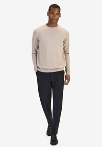 Ljusbeige tröja med rundad hals och ribbade ärmslut, tillsammans med mörkblå byxor och svarta skor, vilket ger en strömlinjeformad silhuett.