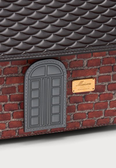 Détail de sac en cuir brun foncé matelassé, motif brique, fenêtre grise en arc et plaque dorée de la marque Maison Moschino.