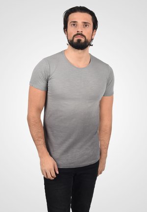 Camisa gris de manga corta, cuello redondo, tela ligera, ligeramente más oscura en la parte inferior. Combinada con jeans negros. Diseño simple y ajustado.