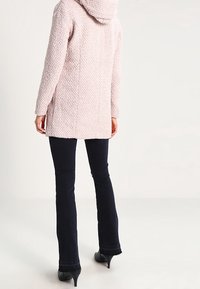 Lichtroze, gestructureerde capuchonjas met lange mouwen, tot halverwege het bovenbeen, met een rechte snit en een gezellige uitstraling. Draag het met donkere jeans.