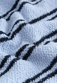 Pruhovaný uterák s textúrovaným povrchom, ktorý má svetlomodré a tmavomodré pruhy. Mäkký, savý materiál sa vlní v záhyboch.