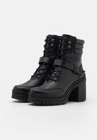 Botas de tobillo negras con un tacón grueso, que presentan un diseño de cordones en la parte frontal, detalle de correa, cuello acolchado y suela de goma texturizada. Material de cuero duradero.