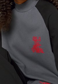 Grå sweatshirt med svarta ärmar, med hög krage och en röd broderad "Quiksilver"-logotyp på bröstet. Mjuk tygtextur.