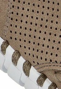 Material de gamuza marrón con textura perforada, suela de goma blanca y cordones marrones contrastantes. Presenta pequeños orificios para permitir la transpiración.