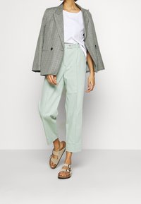 Blazer de cuadros gris de corte oversized, camiseta blanca, pantalones de pierna ancha en menta clara y sandalias beige con hebillas. Textura plana y ajuste relajado.