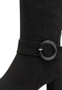 Stivaletto in suede nero con una fibbia circolare in tono argentato su una larga fascia e un design affusolato che si estende verso un tacco alto.