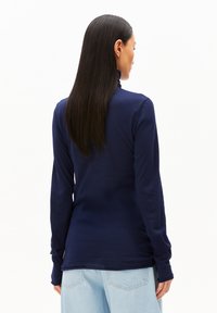 Marineblaues Langarm-Turtleneck-Oberteil aus weichem Stoff, mit tailliertem Design und verlängerten Ärmeln mit Bündchen, von hinten betrachtet.