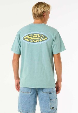 Mint green cotton t-shirt featuring a large yellow graphic logo on the back, with short sleeves and a relaxed fit. Denim shorts are worn.