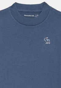 Blaues Baumwoll-T-Shirt mit einem gerippten Rundhalsausschnitt und einem kleinen gestickten Elch-Logo auf der linken Brust. Nahtloses Design mit weicher Textur.