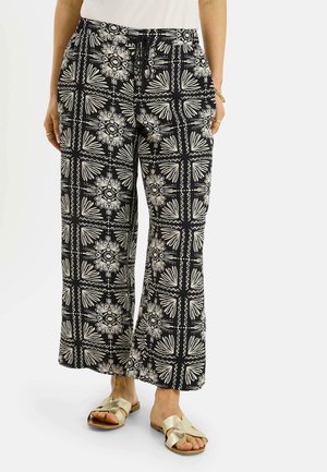 Pantalones anchos con estampado en blanco y negro con diseños florales y geométricos, combinados con sandalias doradas de poner y quitar y una camiseta blanca metida por dentro.