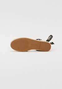 Espadrille sandal med en tan gummisåle, vevd jute-mellomsåle og dekorative svarte og hvite mønstrede tekstilstropper.
