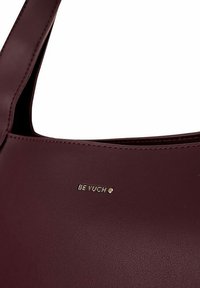 Burgundy leather tote bag with a smooth texture and minimalistic design, featuring embossed gold logo "BE VUCH" on the front.